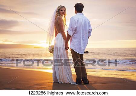Stock Photograph - Married couple, bride and groom at sunset on beautiful tropical beach in Hawaii. Fotosearch