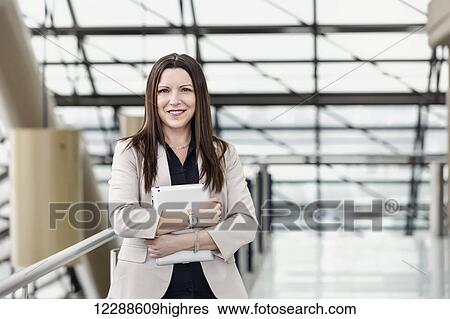 Stock Photograph - Mature business woman posing in an atrium and holding a tablet; Edmonton, Alberta, Canada. Fotosearch