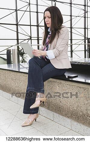 Mature business woman sitting down and looking at a tablet in the atrium of an office building; Edmonton, Alberta, Canada View Large Photo Image Stock Photograph - Mature business woman sitting down and looking at a tablet in the atrium of an office building; Edmonton, Alberta, Canada. Fotosearch