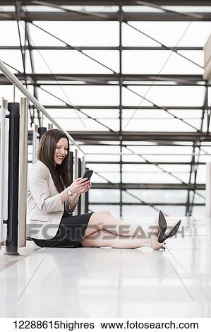 Stock Photograph - Mature business woman sitting down during a break and texting on her smart phone; Edmonton, Alberta, Canada. Fotosearch