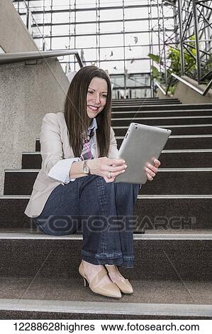 Mature business woman sitting on stairway in the atrium of an office building looking at her tablet; Edmonton, Alberta, Canada View Large Photo Image Stock Photograph - Mature business woman sitting on stairway in the atrium of an office building looking at her tablet; Edmonton, Alberta, Canada. Fotosearch