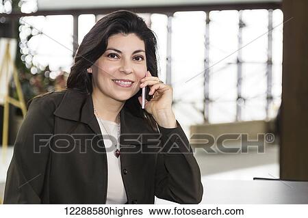 Stock Photograph - Mature business woman talking on her cell phone while taking a break in the atrium of an office building; Edmonton, Alberta, Canada. Fotosearch