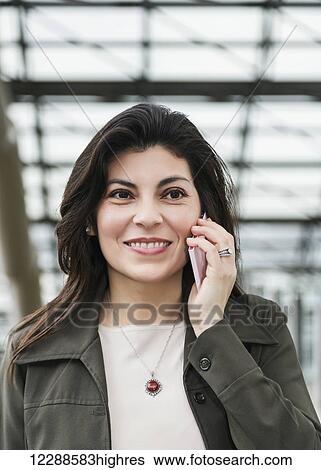 Stock Photograph - Mature business woman talking on her cell phone while taking a break in the atrium of an office building; Edmonton, Alberta, Canada. Fotosearch