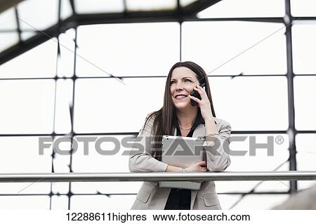 Mature business woman talking on her smart phone and holding a tablet in the atrium of an office building; Edmonton, Alberta, Canada View Large Photo Image Stock Photograph - Mature business woman talking on her smart phone and holding a tablet in the atrium of an office building; Edmonton, Alberta, Canada. Fotosearch