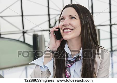 Stock Photograph - Mature business woman talking on her cell phone in the atrium of an office building; Edmonton, Alberta, Canada. Fotosearch