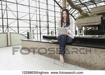 Stock Photograph - Mature business woman with a tablet in the atrium of an office building; Edmonton, Alberta, Canada. Fotosearch