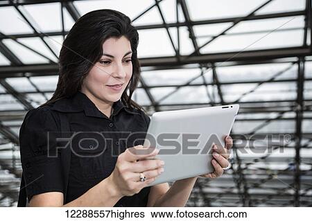 Stock Photograph - Mature businesswoman using her touch screen pad in the atrium of an office building; Edmonton, Alberta, Canada. Fotosearch