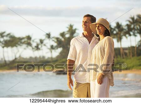 Stock Photograph - Mature Retired Couple Enjoying Sunset on Beach Vacation. Fotosearch