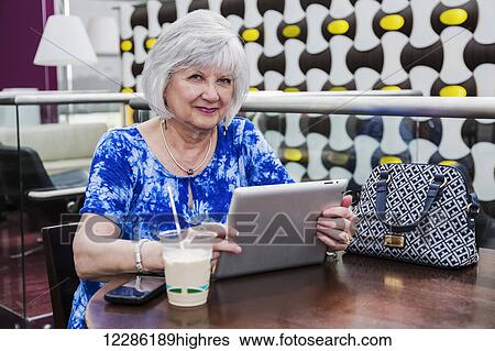 Stock Photograph - Mature woman using her tablet while taking a coffee break at a cafeteria; St. Albert, Alberta, Canada. Fotosearch