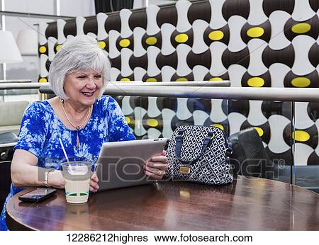 Stock Photograph - Mature woman using her tablet while taking a coffee break at a cafeteria; St. Albert, Alberta, Canada. Fotosearch
