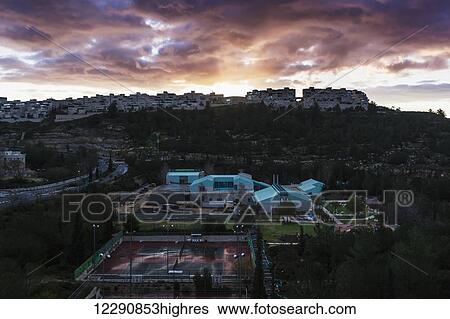 Stock Photograph - Modern buildings and tennis courts under glowing clouds at sunset; Israel. Fotosearch