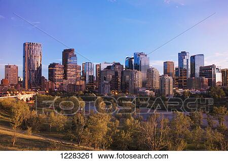 Stock Image - Modern city skyline at sunset with lit skyscrapers; Calgary, Alberta, Canada. Fotosearch