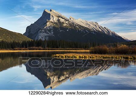 Stock Photograph - Mountain lake reflecting mountain at sunset with blue sky and clouds, Banff National Park; Alberta, Canada. Fotosearch