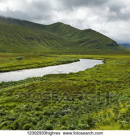 Mountains and fields covered in green foliage with a river running through it under a cloudy sky in the Highlands; Scotland View Large Photo Image Stock Photograph - Mountains and fields covered in green foliage with a river running through it under a cloudy sky in the Highlands; Scotland. Fotosearch