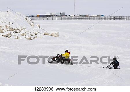 Native Alaskan youth on a snowmachine towing another on sled, City of Barrow in the background, North Slope, Arctic Alaska, USA, Winter View Large Photo Image Stock Photograph - Native Alaskan youth on a snowmachine towing another on sled, City of Barrow in the background, North Slope, Arctic Alaska, USA, Winter. Fotosearch
