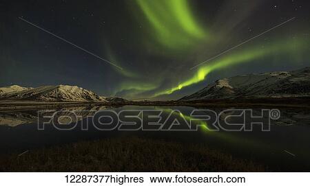 Stock Photograph - Northern Lights (aurora borealis) over the Dempster Highway and reflected into a pond; Yukon, Canada. Fotosearch