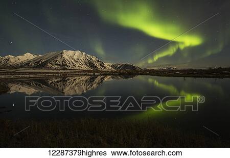 Stock Photograph - Northern Lights (aurora borealis) over the Dempster Highway and reflected into a pond; Yukon, Canada. Fotosearch
