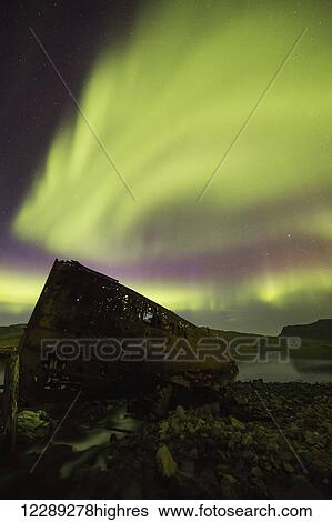 Stock Photograph - Northern lights over top of the town known as Djupavik along the Strandir Coast, here they are dancing above the old herring factory and shipwreck; Djupavik, Iceland. Fotosearch