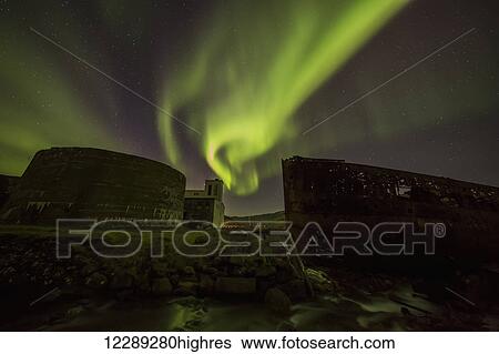 Stock Photograph - Northern lights over top of the town known as Djupavik along the Strandir Coast, here they are dancing above the old herring factory and shipwreck; Djupavik, Iceland. Fotosearch