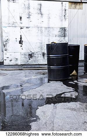 Stock Photograph - Oil Barrels in an industrial site leaking across the pavement; Vancouver, British Columbia, Canada. Fotosearch