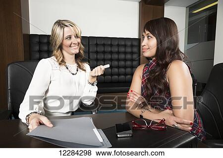 Stock Photo - One professional business woman handing a thumb drive to a co-worker during a meeting; St. Albert, Alberta, Canada. Fotosearch