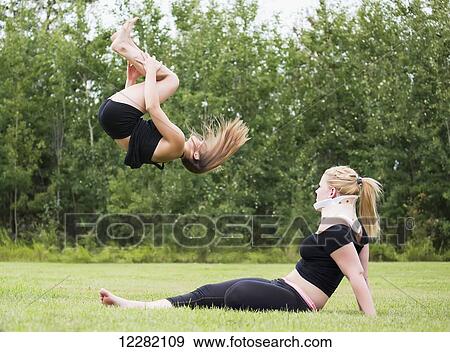 One teenage gymnast practicing her back tuck outdoors in a park while her injured partner watches; Edmonton, Alberta, Canada View Large Photo Image Stock Photo - One teenage gymnast practicing her back tuck outdoors in a park while her injured partner watches; Edmonton, Alberta, Canada. Fotosearch
