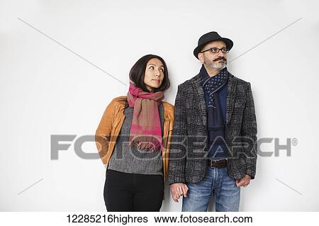Stock Photograph - Persian man and Tibetan woman holding hands and leaning against a wall, man looking away while woman is looking at man; Toronto, Ontario, Canada. Fotosearch
