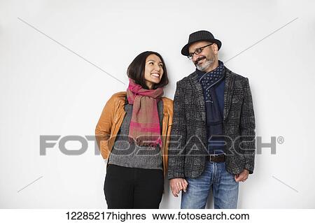 Stock Photograph - Persian man and tibetan woman leaning against a wall smiling and holding hands; Toronto, Ontario, Canada. Fotosearch