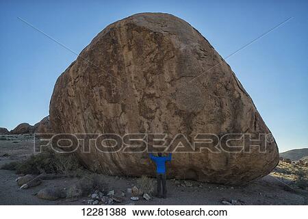 Stock Photo - Person standing under a large boulder in Richtersveld National Park; South Africa. Fotosearch