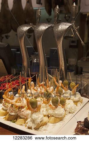 Stock Photograph - Pintxos of prawn, crab, olive and egg on a slice of bread on a bar counter in front of a set of beer taps; San Sebastian, Spain. Fotosearch