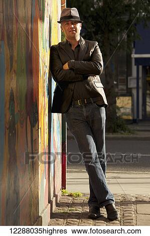 Stock Photograph - Portrait of a man in a hat leaning against a sunlit wall; London, England. Fotosearch
