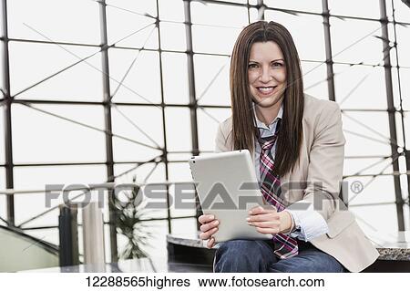 Stock Photograph - Portrait of a mature business woman with a tablet in the atrium of an office building; Edmonton, Alberta, Canada. Fotosearch