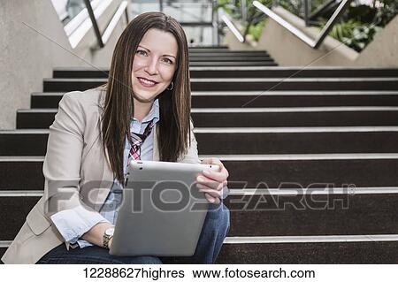 Portrait of a mature business woman sitting on stairway in the atrium of an office building with a tablet; Edmonton, Alberta, Canada View Large Photo Image Stock Photograph - Portrait of a mature business woman sitting on stairway in the atrium of an office building with a tablet; Edmonton, Alberta, Canada. Fotosearch