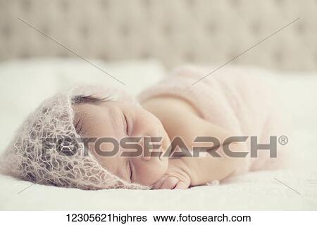 Stock Photograph - Portrait of a newborn baby laying on a bed with white comforter; Toronto, Ontario, Canada. Fotosearch