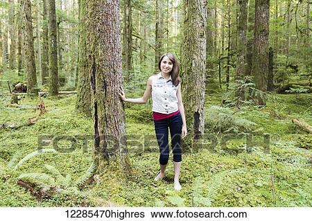 Stock Photograph - Portrait of a teenage girl leaning against a tree in a forest; Chilliwack, British Columbia, Canada. Fotosearch