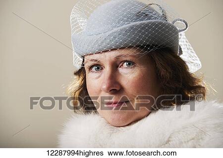 Stock Photograph - Portrait of a woman with brunette hair wearing a blue veiled hat and white fur; Caldecott, England. Fotosearch