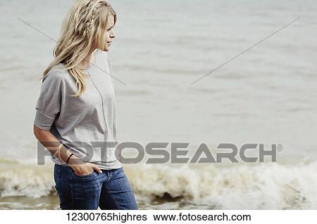 Stock Photograph - Portrait of a young woman with long blond hair at the ocean; Hastings, Sussex, England. Fotosearch