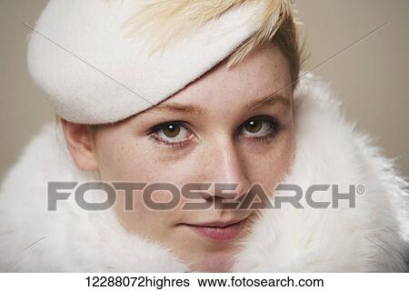 Stock Photograph - Portrait of a young woman with red hair in a white hat and white fur; Caldecott, England. Fotosearch