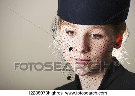 Stock Photograph - Portrait of a young woman with red hair in a black veiled hat; Caldecott, England. Fotosearch