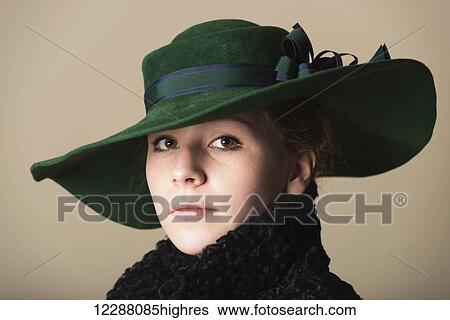 Portrait of a young woman with red hair looking serious in a black overcoat with the collar turned up and a green wide-brimmed hat with a blue and green ribbon; Leicestershire, England View Large Photo Image Stock Photograph - Portrait of a young woman with red hair looking serious in a black overcoat with the collar turned up and a green wide-brimmed hat with a blue and green ribbon; Leicestershire, England. Fotosearch