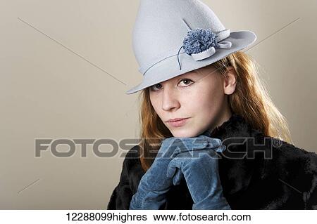 Stock Photograph - Portrait of a young woman with red hair wearing a blue hat and black fur coat and leaning on blue gloved hands; Caldecott, England. Fotosearch