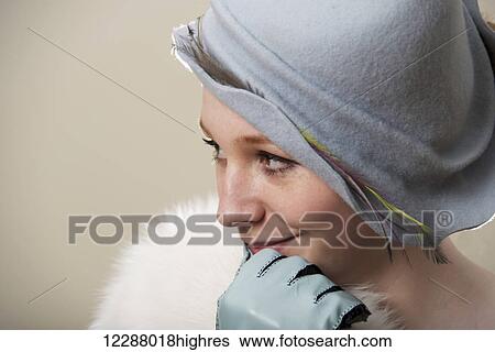 Stock Photograph - Portrait of redhead in white fur and blue hat with gloved hand at her mouth; Caldecott, England. Fotosearch