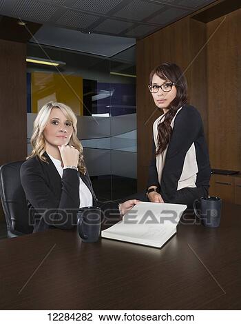Stock Image - Portrait of two professional business women during a casual meeting in a boardroom; St. Albert, Alberta, Canada. Fotosearch