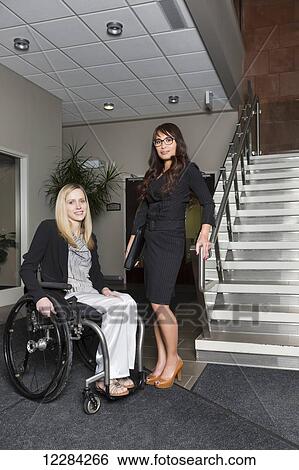 Stock Photograph - Portrait of two professional business women in the lobby of an office, one of which is a paraplegic in a wheelchair; St. Albert, Alberta, Canada. Fotosearch