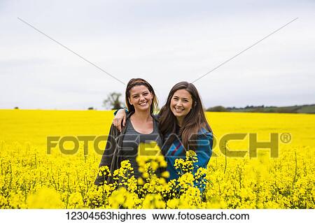 Portrait of two young women standing in a field covered in vibrant yellow Rapeseed flowers; Cotswolds, England View Large Photo Image Stock Photograph - Portrait of two young women standing in a field covered in vibrant yellow Rapeseed flowers; Cotswolds, England. Fotosearch