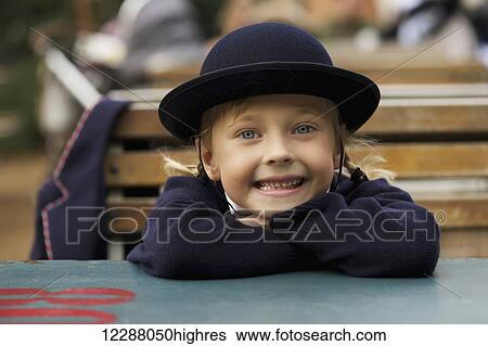 Stock Photograph - Portrait of young girl wearing school uniform, sitting and smiling; London, England. Fotosearch