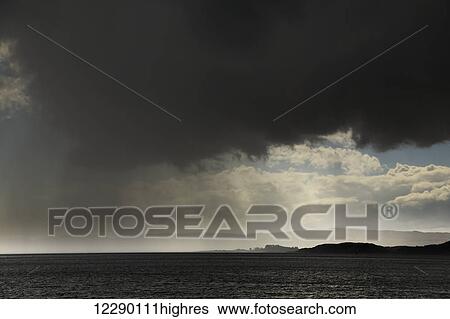 Stock Photograph - Rain falling from ominous dark clouds over the water; Otter Ferry, Scotland. Fotosearch