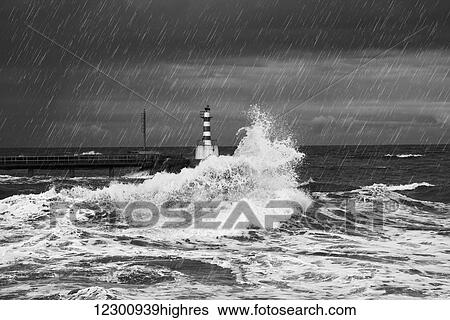 Stock Photograph - Rainfall and splashing waves with a lighthouse along the coast; Amble, Northumberland, England. Fotosearch
