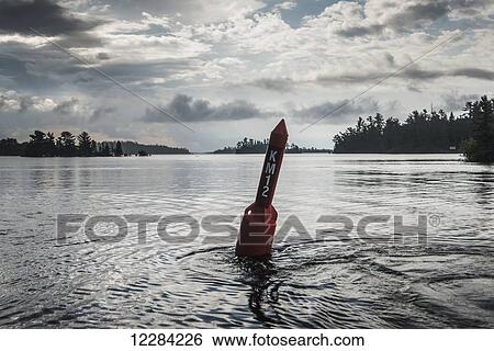 Stock Photograph - Red buoy in a lake with letters and numbers; Ontario, Canada. Fotosearch