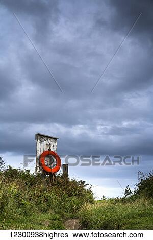 Stock Photograph - Red ring life preserver hanging on a wooden post; Northumberland, England. Fotosearch